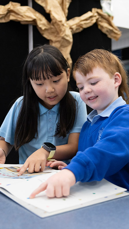 St Canice's student being assisted by Year 6 buddies. The student is writing in his booklet.