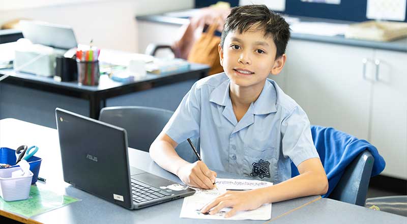 St Canice’s Katoomba student writing in workbook and studying from laptop