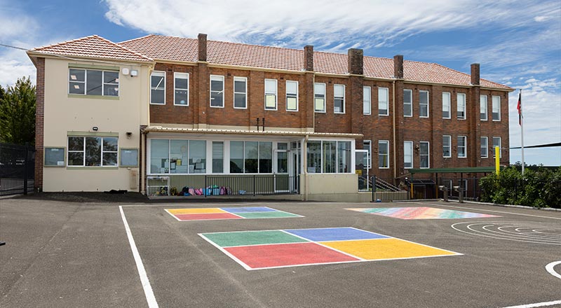 St Canice's Katoomba School grounds. The photo features the school building, playground, flagpole, and painted handball courts.