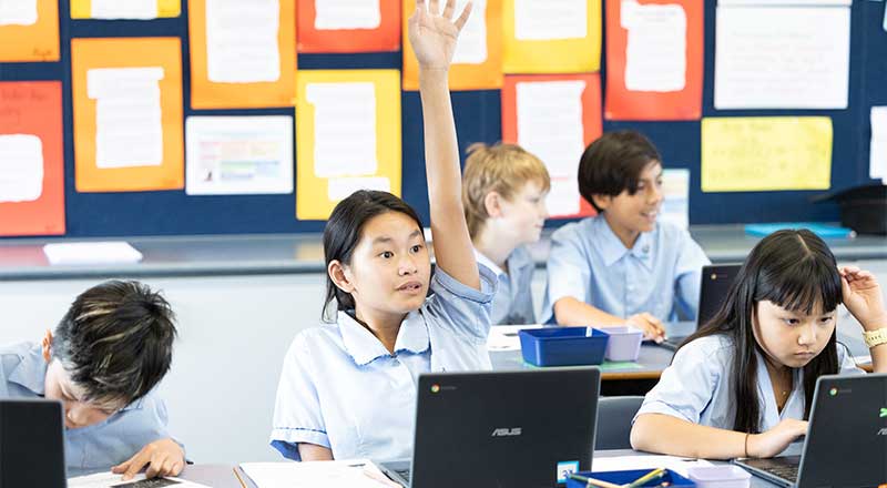 St Canice’s Katoomba students in class - The students have their hands raised, and are also researching using their laptops.
