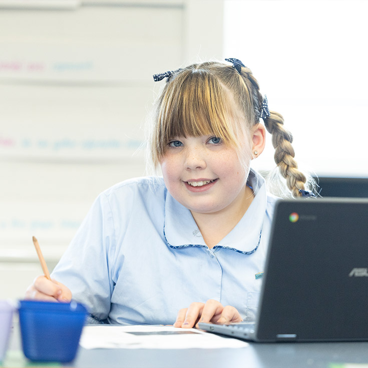 St Canice's Katoomba student in class. She is holding a pencil, using a laptop and writing in a workbook
